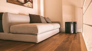 Una sala de estar moderna con un sofá, piso de madera, un cuadro en la pared y un cubo de basura.