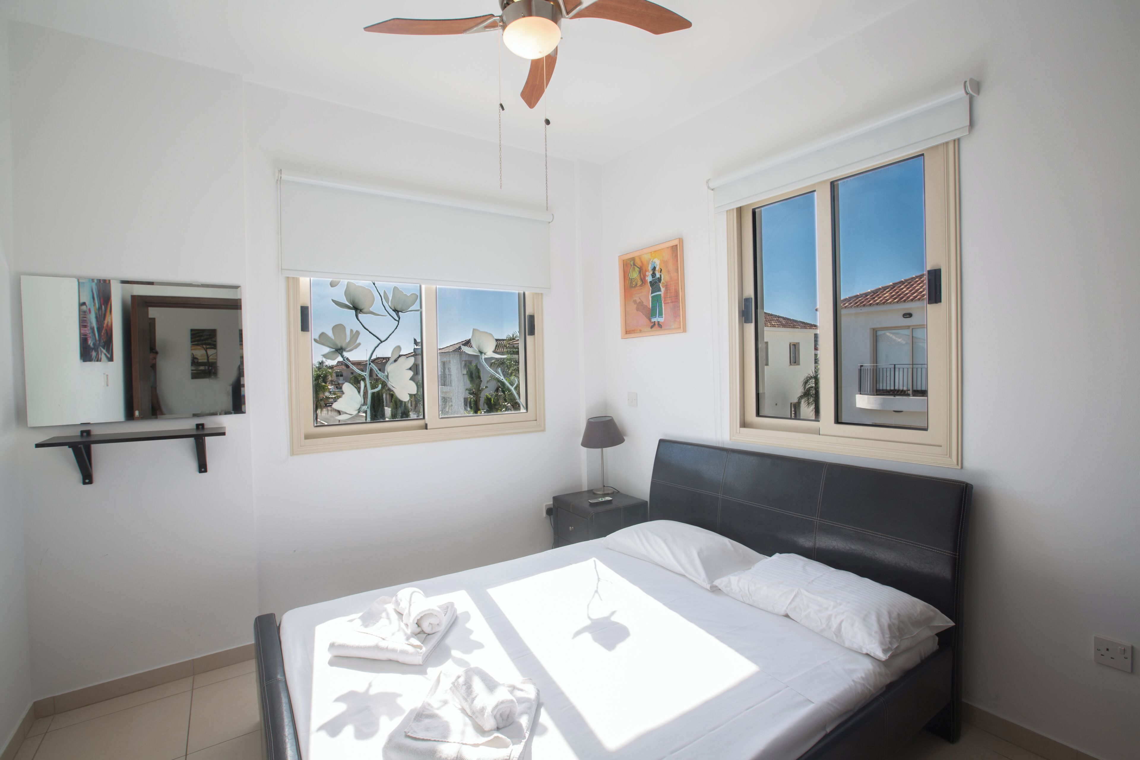 Une chambre à coucher avec un lit, un ventilateur de plafond, une fenêtre donnant sur un beau paysage et une table de chevet avec une lampe.