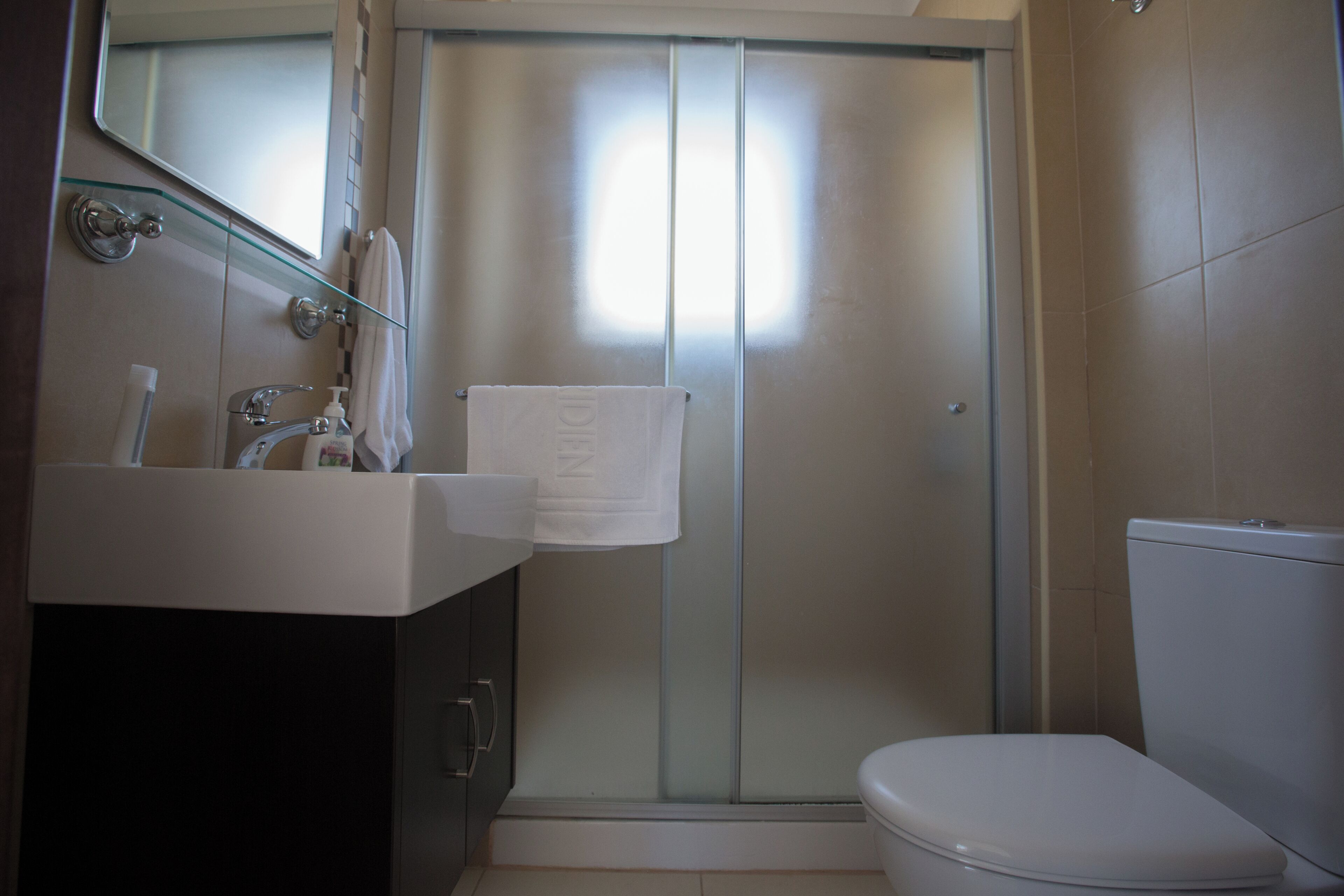Ein Badezimmer mit Duschkabine aus Glas, einem weißen Waschbecken und einer Toilette.