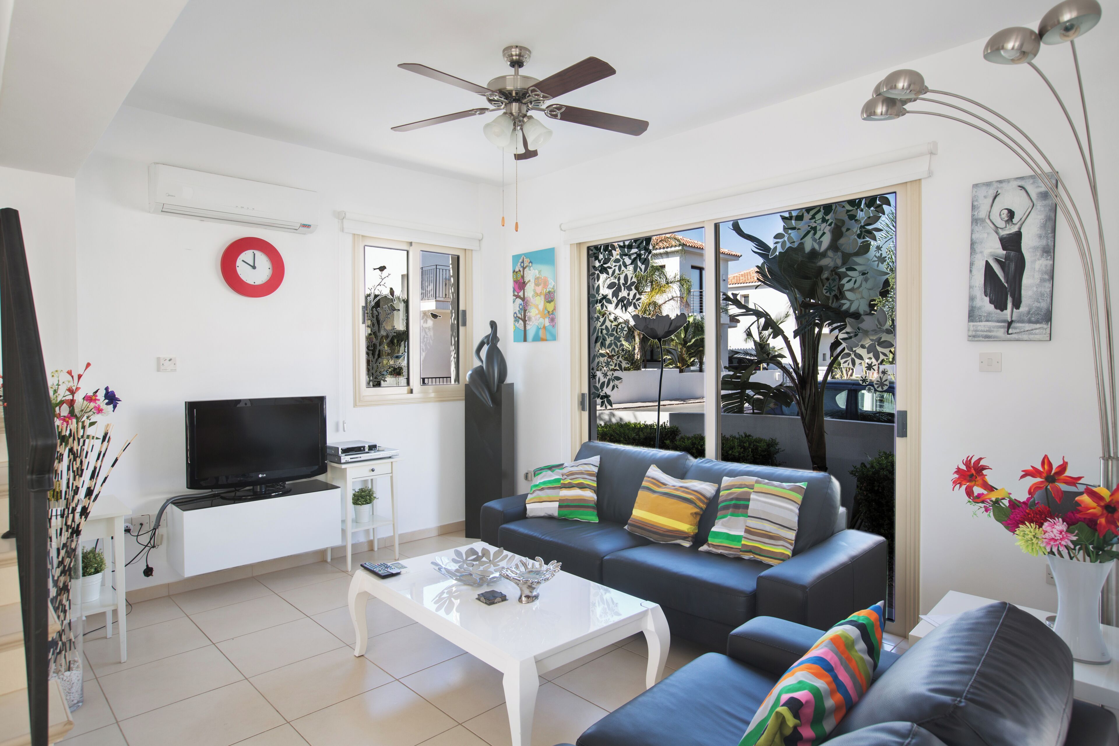 A modern living room with a flat-screen TV, a ceiling fan, a sofa, and a coffee table.