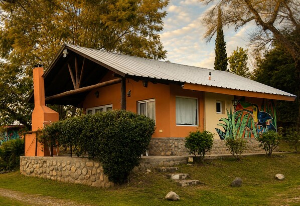 A house with a sloped roof, a chimney, and a stone wall in front.