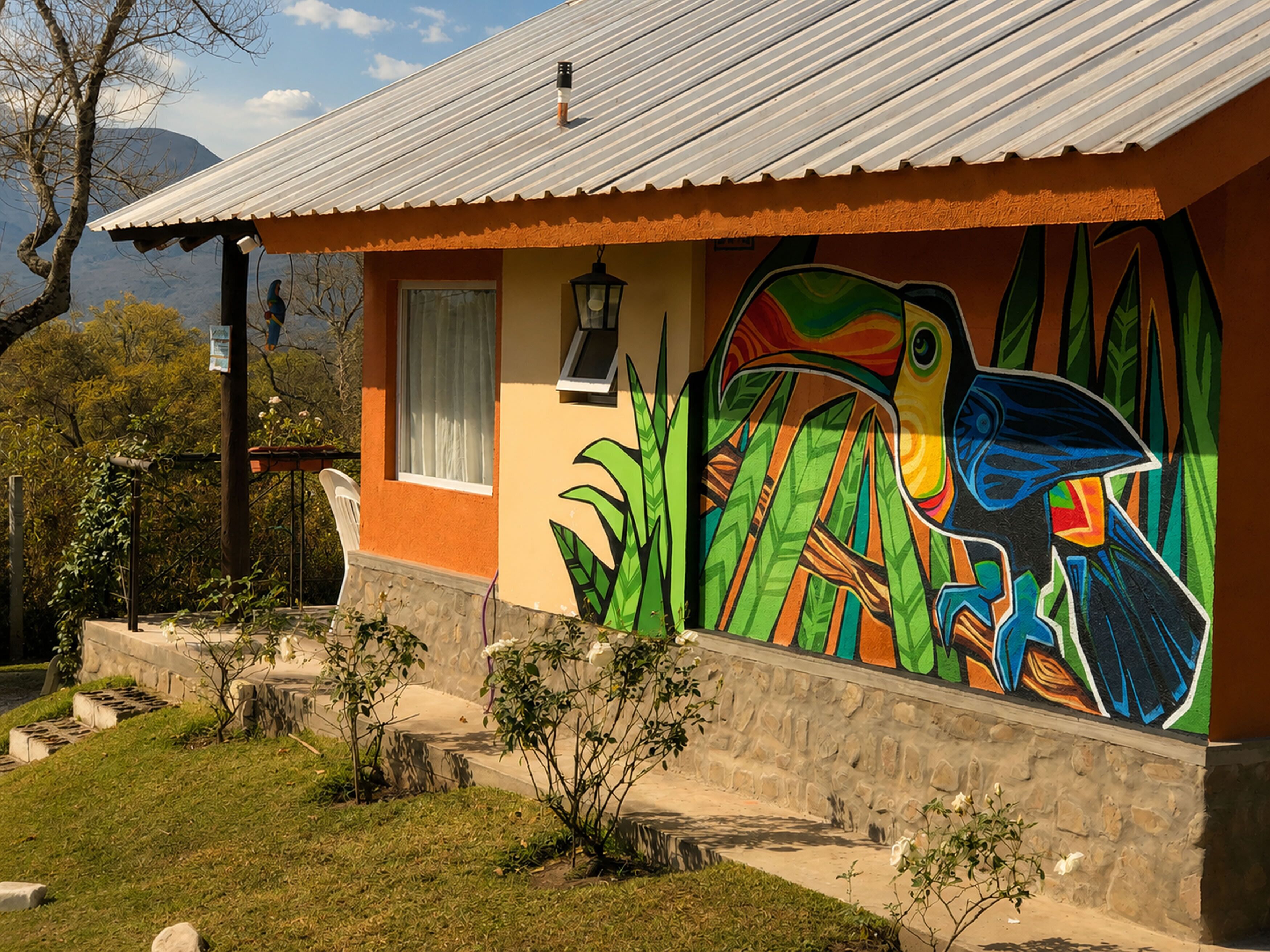 A house with a colorful mural of a bird and foliage, a white window, and a metal roof.