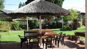 An outdoor patio with a thatched umbrella, a wooden table, and chairs. - Casa Villa Guest House Carletonville - Suite 4 (Merafong City)