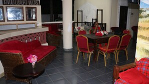A dining area with a round table and red upholstered chairs, a wicker sofa, and a small table with a vase of flowers. - Room-a Wonderful Beach Property in Diani (Mombasa)