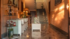 Un pasillo con un expositor de vidrio, muebles de mimbre, una pequeña mesa con un farol y una escalera.