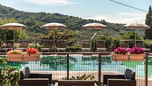 Zona junto a la piscina con sillones y sombrillas, rodeada por una valla, con vistas a la piscina y un paisaje montañoso.