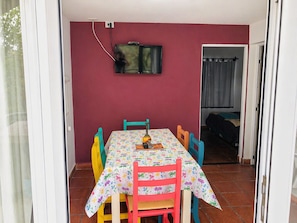 A dining area with a table and chairs, a television mounted on the wall, and a door leading to another room.