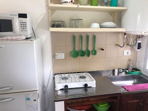 Een keuken met een witte koelkast, een magnetron, een gasfornuis en een spoelbak.