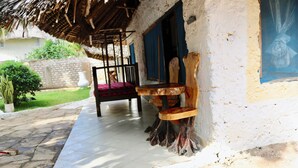 A rustic outdoor seating area with a wooden bench and a chair, a thatched roof, and a white exterior wall. - Room-a Wonderful Beach Property in Diani (Mombasa)