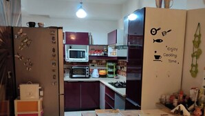 A compact kitchen with a microwave, toaster, and gas stove. A ceiling fan is visible, and there are colorful storage boxes. - Room-'mount View Double-bed' By Aparna B (Kalka)