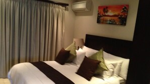 Ein Hotelzimmer mit einem großen Bett, einem Kopfteil, einem Gemälde an der Wand und einer Klimaanlage.