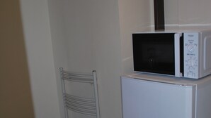 A compact kitchenette with a white refrigerator, a microwave, and three plastic bins.