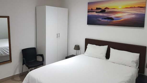 A hotel room with a bed, a wardrobe, a chair, a nightstand, a lamp, and a painting of a sunset. - Room-relaxing Guest House in the Heart o (Cape Town)