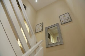 Staircase leads to an upper floor, flanked by framed artworks and a large mirror.