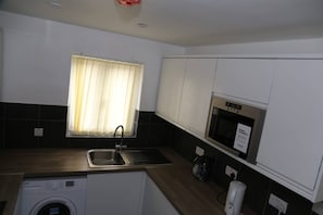 Compact kitchen with a washing machine, sink, and microwave, offering a convenient space for meal preparation.