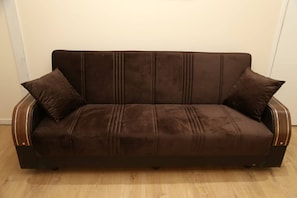 A comfortable sofa with a wooden frame and matching cushions sits against a wall.