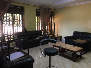 A living room with a sofa, a chair, a coffee table, and a TV stand. - Room-private Room With Jacuzzi in Kigali (Kigali)