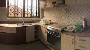 A kitchen with a gas stove, oven, sink, and a window with a metal grill. - Room-private Room With Jacuzzi in Kigali (Kigali)