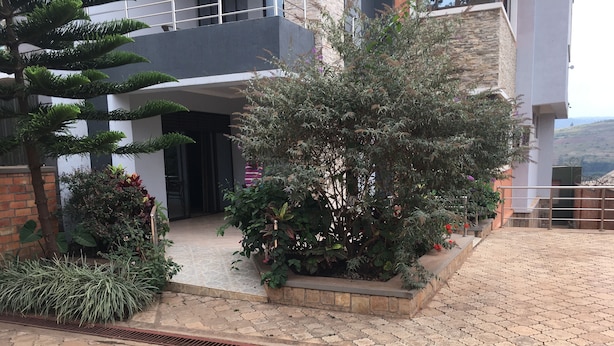 Un bâtiment moderne doté d’une entrée pavée, d’un petit jardin agrémenté de diverses plantes et d’un portail en métal.