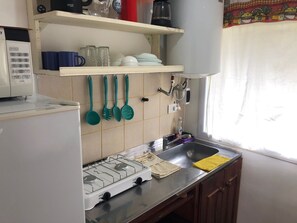 A kitchen with a gas stove, a sink, and various utensils hanging on the wall. - Mama Pacha Cabin Rural Nature Retreat Near Salta (Vaqueros)