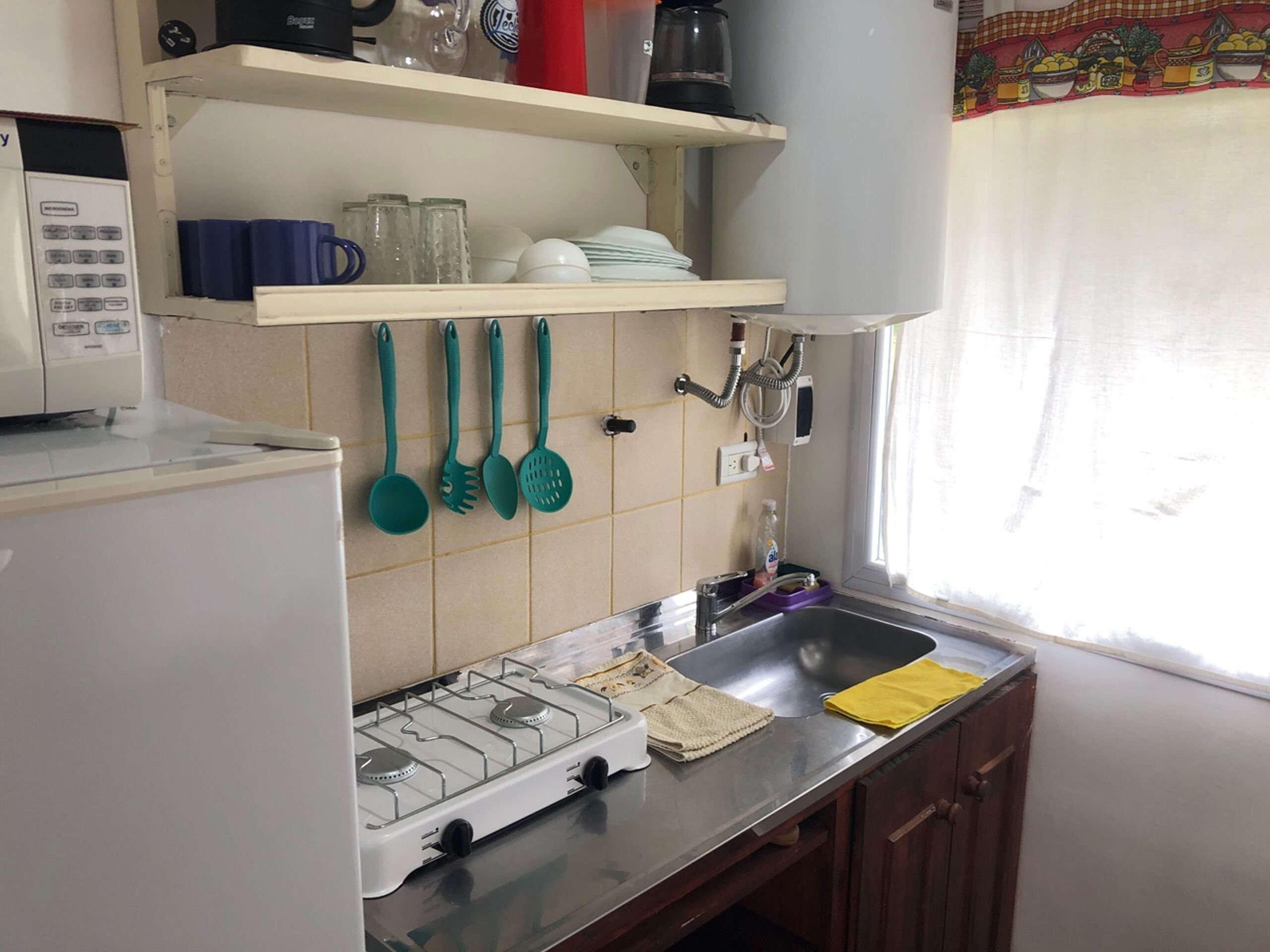 A kitchen with a gas stove, a sink, and various utensils hanging on the wall.