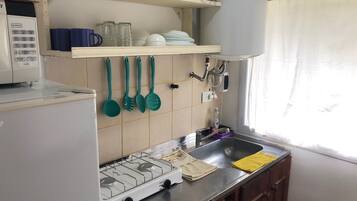 A kitchen with a gas stove, a sink, and various utensils hanging on the wall.