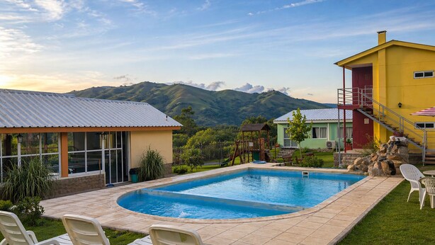 A swimming pool with lounge chairs, a small building with a metal roof, and a view of mountains. - Mama Pacha Cabin Rural Nature Retreat Near Salta (Vaqueros)