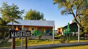 A colorful building with a mural, a sign reading 'CABANAS WARA-KUSI,' and a fenced area with trees. - Mama Pacha Cabin Rural Nature Retreat Near Salta (Vaqueros)