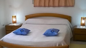 A bedroom with a bed, two bedside lamps, a painting on the wall, and a window with curtains. - Sa Domu Sarda - Two Bedroom Apartment 1 (Piscinas)