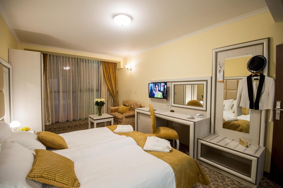 Quarto de hotel com uma cama grande, uma escrivaninha com computador, televisão e espelho.