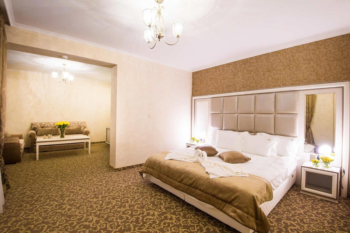 A hotel room with a large bed, a bedside table, a chair, and a small table with flowers.