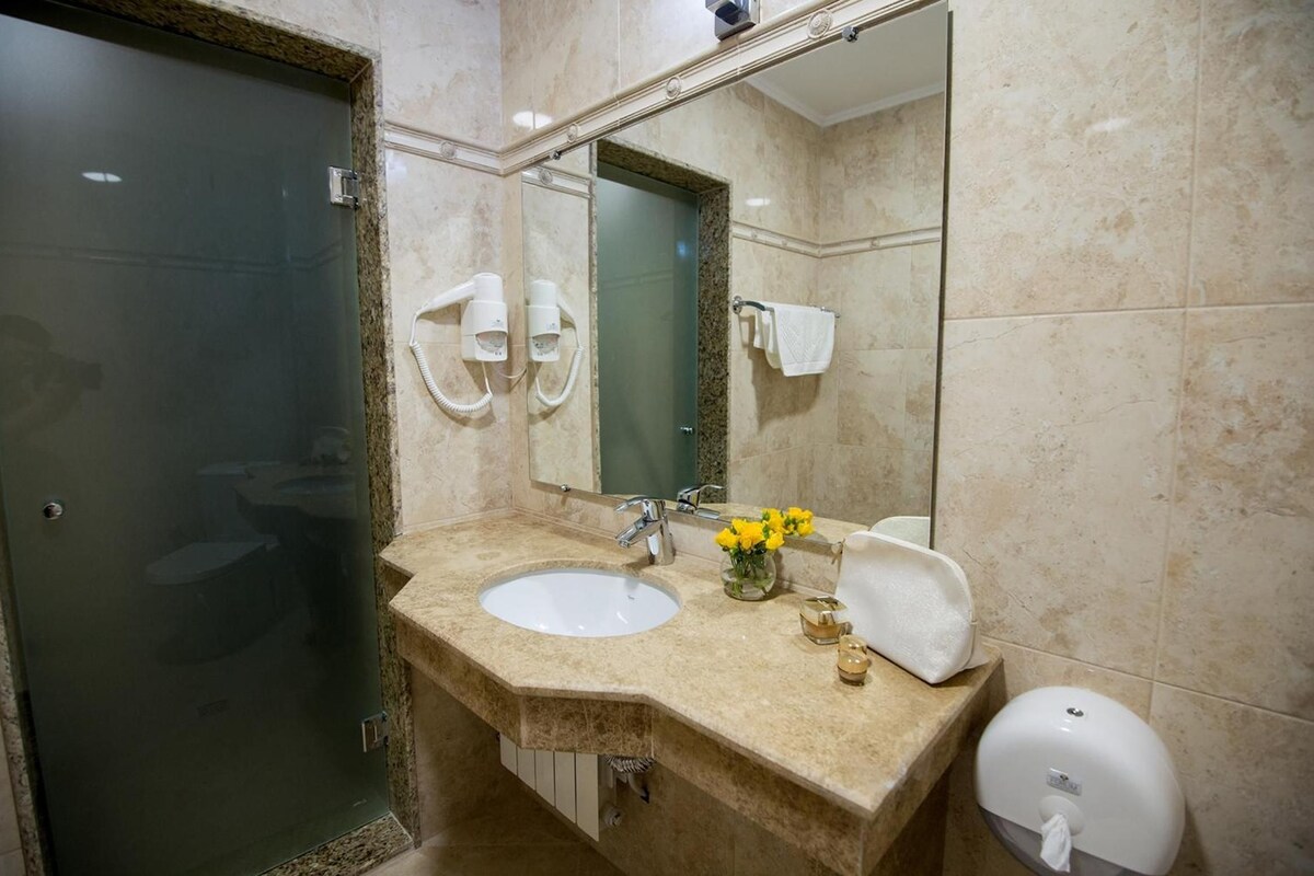 Casa de banho com lavatório, espelho, porta-toalhas e secador de mãos.