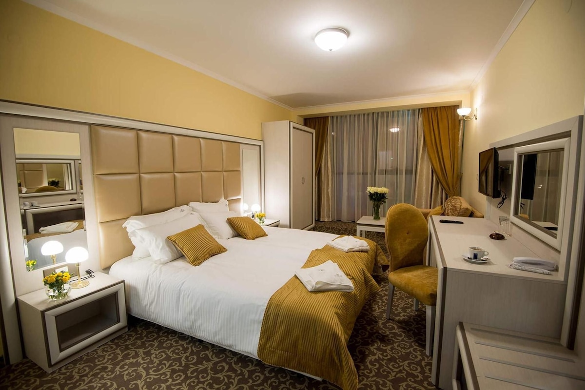 A hotel room with a large bed, a desk, a chair, a mirror, and a television.
