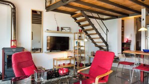 Een moderne woonkamer met een televisie, rode stoelen, een glazen tafel en een houten trap.