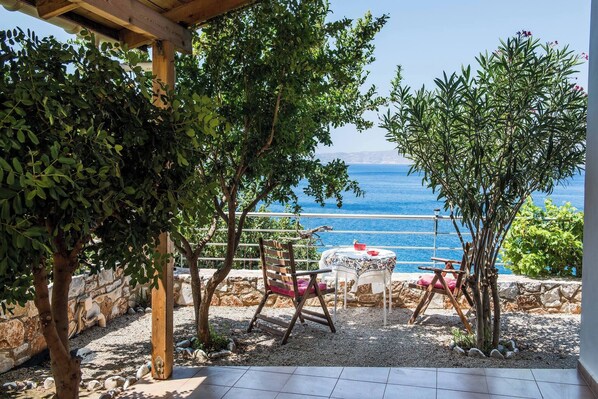A patio with a table and chairs, a view of the sea, and a stone wall.