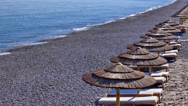 Een strand met rijen ligbedden en rieten parasols.