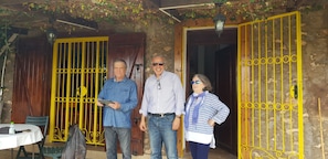 Tres personas de pie frente a un edificio con puertas amarillas y una mesa con una botella y una bolsa.