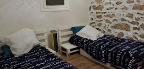 Un dormitorio con dos camas individuales, una mesita de noche pequeña, un calentador y una pared con diseño de piedra.