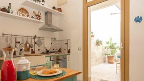 A kitchen with a wooden table, a red bottle, and a plate with food. There are shelves above the counter with kitchen items. - Little Home Holidays (Vernole)