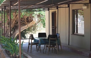 A covered outdoor seating area with a table and chairs, a tree, and a window. - Room-confortable Farmhouse in Limpopo Pr (Lephalale)