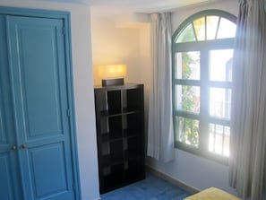 Een kamer met een blauwe deur, een zwarte plankkast, een raam met gordijnen en een geel bed.