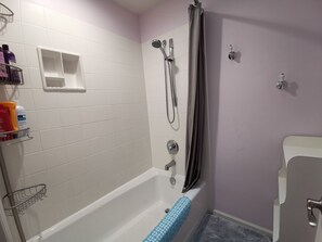 A bathroom with a bathtub, shower, and toilet. There are toiletries on a shelf and a towel rack. - Nature House3 Rooms (Issaquah)