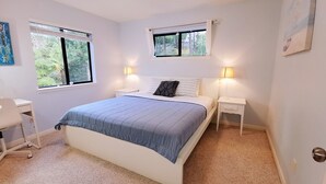 A bedroom with a bed, two bedside tables, a desk, and two windows.