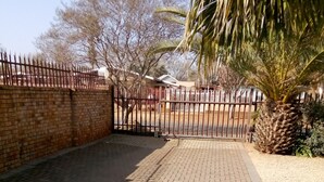 A paved courtyard with a brick wall, a metal gate, and a palm tree. - Casa Villa Guest House Carletonville - Suite 2 (Merafong City)