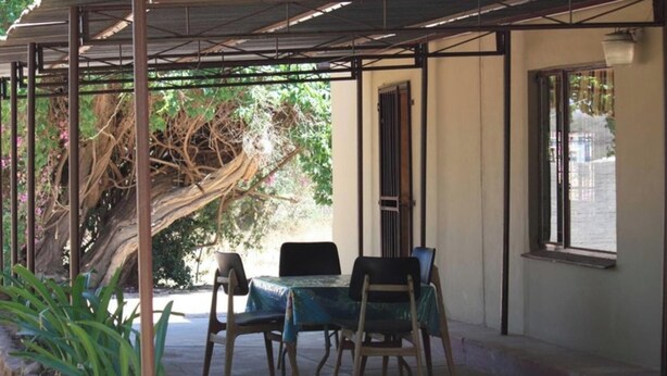 Un espacio al aire libre cubierto con mesa y sillas, un árbol y una ventana.