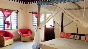 A room with a bed, two wicker chairs, a ceiling fan, and a window with curtains.