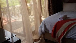 A bedroom with a bed, a TV, and a view of the outdoors through sheer curtains.