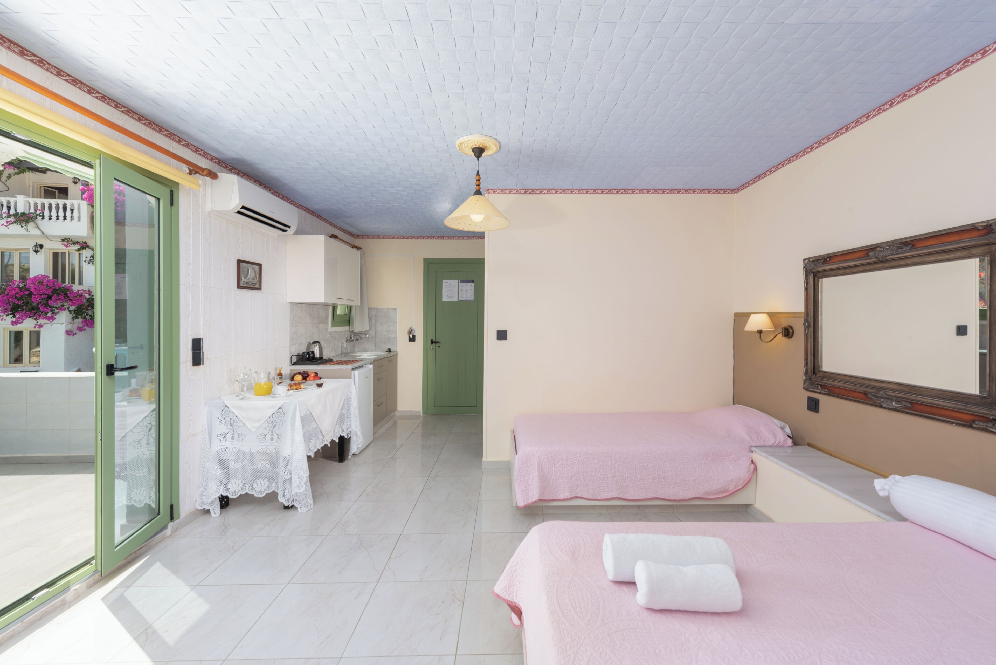 Habitación de hotel con dos camas, baño, kitchenette y balcón con flores.