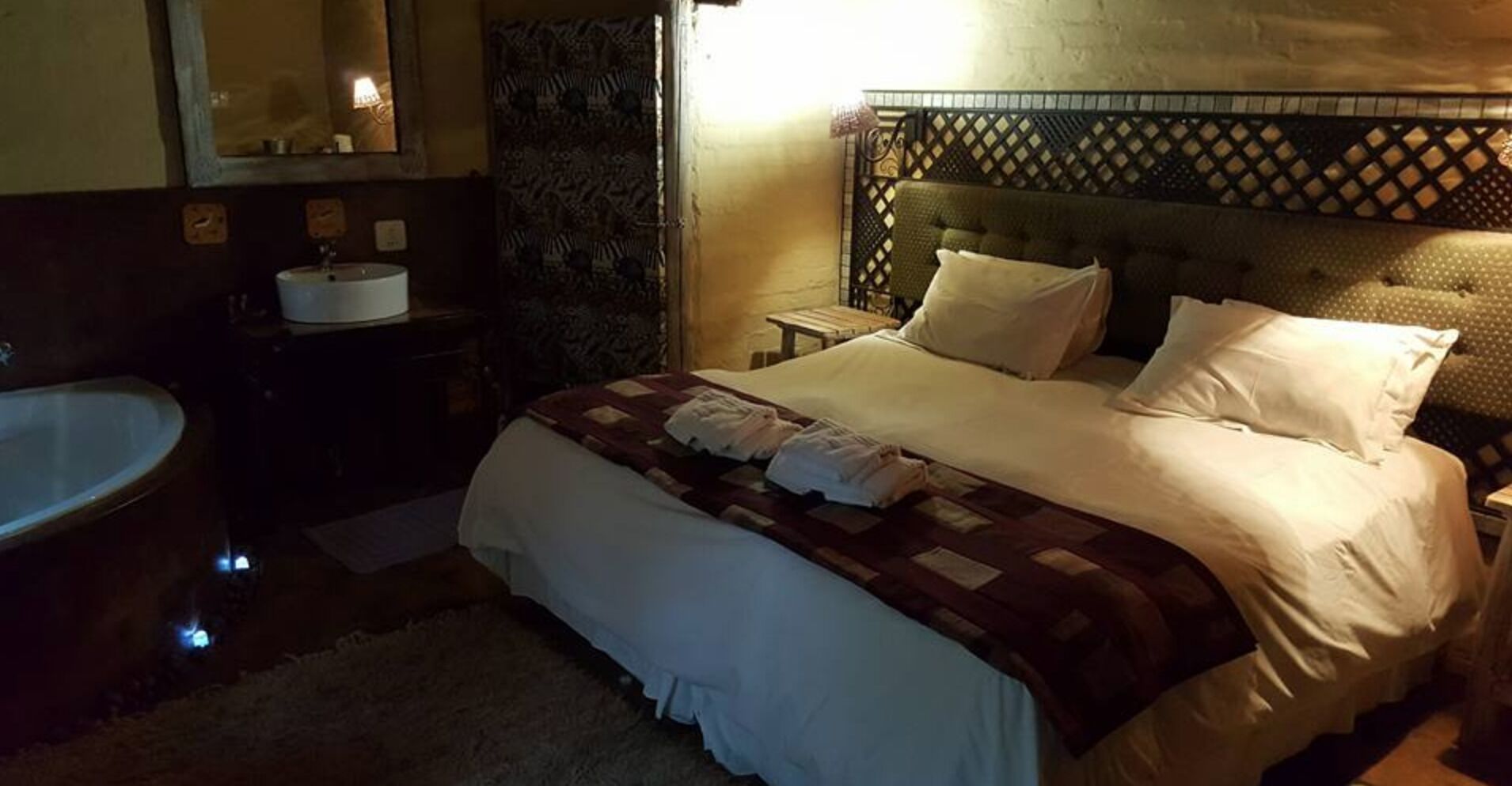A hotel room with a large bed, a bedside table, a nightstand, a sink, and a mirror.