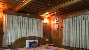 A wooden cabin bedroom with a bed, curtains, a nightstand, and a wall-mounted lamp. - Luxury Private Villa with Mountain View (Banjar)
